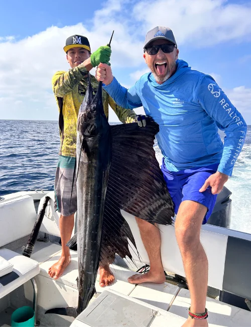 Two individuals holding a sailfish on an offshore fishing boat