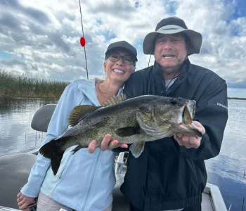 A couple holding a largemouth bass on a boat