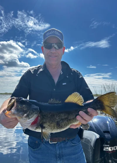 Largemouth bass held on calm water under a blue sky